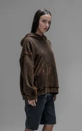 Hoodie de corte oversize y largo crop, confeccionado en algodón con efecto de desgaste y color óxido. Presenta costuras expuestas, detalles de roturas en los bordes y bolsillo frontal tipo canguro.