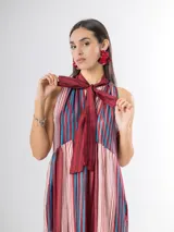Vestido largo de corte halter en organdí, con estampado de rayas verticales y horizontales en tonos bordó, azul y crudo. Cuenta con un lazo en el cuello y un volado en la parte inferior.