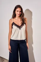 Blusa de satén color marfil con detalles de encaje negro en el escote en V y en el ruedo, de tirantes finos y corte recto.