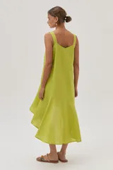Vestido de lino color lima, corto al frente y más largo en la espalda, con volado en el bajo que aporta movimiento y frescura.