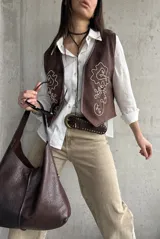 Chaleco de gamuza color marrón chocolate, con diseño sin mangas y escote en V. Cuenta con bordados en hilo claro y pequeños detalles de tachas en la parte frontal.