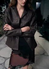 Blazer de cuero ovino color marrón oscuro, con diseño de corte recto, solapas clásicas y cierre frontal con botones a tono.