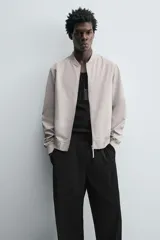 Cazadora bomber ligera de tejido técnico color verde oliva, con cuello, puños y bajo en rib elástico. Presenta cierre frontal de cremallera y bolsillos de vivo en la cadera.