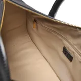 Cartera tipo baúl compacta de símil gamuza color negro, combinada con detalles de PU liso. Cuenta con doble asa corta rígida, correa larga regulable y desmontable, y herrajes metálicos dorados. El compartimento principal tiene cierre superior y un bolsillo interno con cierre. Detalle frontal con logo XL metalizado.