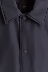 Campera de estilo coach, color azul marino, con cuello inglés, cierre frontal con botones a presión y bolsillos laterales insertados. Presenta puños y bajo con elástico, y cuenta con forro interior acolchado.