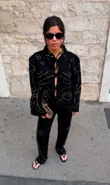 Chaqueta corta de denim negro con cuello clásico y cierre frontal con cordones. Decorada con tachas plateadas formando patrones ondulados.