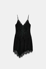 Top de escote en pico con tirantes finos, confeccionado en tejido satinado negro. Presenta bordados decorativos en el frente y un bajo asimétrico con detalle de puntilla de encaje.