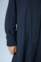 Trench midi negro confeccionado en algodón y nylon repelente al agua, con cuello clásico, cierre cruzado con botones, cinturón ajustable, mangas largas con puños abotonados, bolsillos internos altos y tajos laterales.