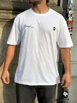 Remera blanca de corte oversize con estampado en la espalda que incluye dos círculos intersecados con las palabras 'Surf', 'Life' y 'Skate', y las frases 'Real Experience', 'Coexist' y 'Meaningful Day'.