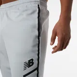 Pantalón de jogging gris claro de New Balance, modelo Tenacity, con logo negro estampado en el muslo izquierdo.