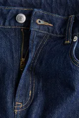 Jean de tiro alto confeccionado en denim de algodón lavado, con diseño de cinco bolsillos y piernas rectas de corte holgado. Cierre frontal con botón y cremallera.