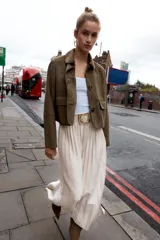 Falda midi plisada de tiro alto color beige, con cinturón a tono y hebilla metálica dorada. Cierre lateral con cremallera oculta.