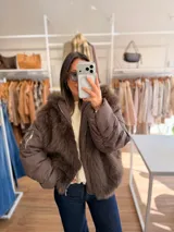 Campera puffer oversize color marrón, con paneles frontales y traseros de pelo sintético suave. Presenta mangas acolchadas, cierre frontal y bolsillo con cierre en la manga.