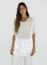Blusa blanca de lino y algodón con cuello redondo y mangas cortas. Diseño holgado con ruedo irregular y detalle de volados.
