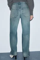 Jeans de tiro medio, corte recto y ancho, en denim azul claro con efecto lavado y desgaste. Presenta cierres metálicos completos a lo largo de las costuras laterales exteriores de ambas piernas.