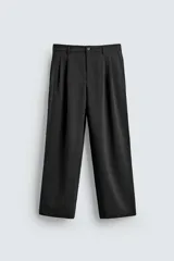 Pantalón de vestir negro, corte ancho, con pliegues frontales dobles, bolsillos laterales y traseros de vivo. Cierre frontal con cremallera y botón.