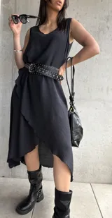 Vestido midi negro sin mangas, con escote redondo y corte asimétrico con volados. Incluye cinturón de cuero con tachas.