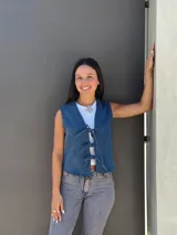 Chaleco de jean azul con cierre frontal mediante lazos ajustables, sin mangas y corte recto.