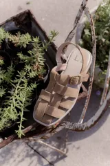 Sandalias de cuero negro con diseño de tiras entrelazadas, estilo huarache, con pulsera ajustable al tobillo mediante hebilla metálica.