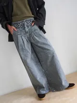 Pantalón wide leg de denim con lavado ácido gris. Presenta una cintura alta con detalle de pasacintas entrelazadas, cierre frontal y bolsillos laterales.