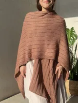 Ruana tejida en punto jersey, color negro con destellos brillantes de lurex. Presenta una etiqueta de cuero sintético con logo en la parte posterior.