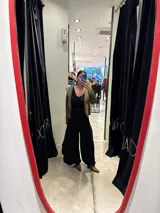 Pantalón de corte amplio y fluido, color gris con acabado satinado, con cintura elástica y lazo ajustable. Presenta un diseño con paneles laterales que aportan volumen y movimiento.