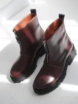 Botas de cuero color marrón con suela track negra y cierre frontal con cremallera roja.