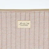 Neceser rectangular acolchado con diseño de rayas horizontales en color beige y blanco. Presenta bordes festoneados, cierre superior metálico y una etiqueta decorativa en el centro.