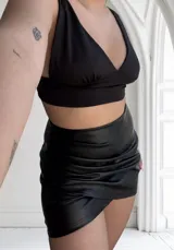 Minifalda negra de cuero sintético con frunces y corte cruzado.