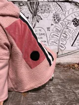 Campera tipo hoodie confeccionada en técnica de collage con texturas combinadas. Presenta cuerpo principal en tejido tipo corderito rosa, con paneles traseros en pana rosa, detalles en franjas verticales blancas y negras, y un aplique circular negro. Incluye capucha integrada.