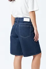 Bermuda de denim color azul oscuro, de corte relajado y largo a la rodilla, con costuras contrastantes en color claro.