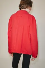 Chaqueta oversize de corte recto en color rojo, con cuello solapa, manga larga y bolsillos de parche delanteros. Cuenta con cierre frontal de botones metálicos y pespuntes a contraste.