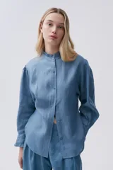 Camisa celeste de lino con cuello mao con volados, mangas largas abullonadas con puños con volados y cierre frontal con botones.