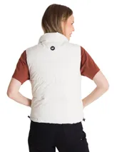 Chaleco puffer corto de color beige, con cuello alto, cierre frontal con cremallera y solapa protectora. Presenta un diseño acolchado, bolsillos laterales con cierre y parche de silicona con logo en la nuca.