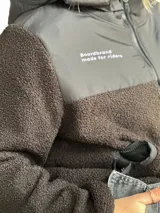 Campera de corderito de manga larga y cierre frontal, con diseño en bloques de color azul y negro. Cuenta con capucha y bolsillos laterales, además de detalles estampados con la marca y la frase 'boardbrand made for riders'.