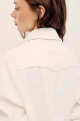 Campera corta de gabardina blanca estilo trucker, con bolsillos frontales con solapa, mangas largas y cierre de botones metálicos.