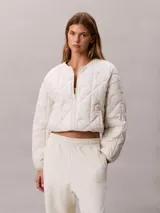 Campera puffer Calvin Klein color beige, de cuello redondo, manga larga y cierre frontal con cremallera blanca. Presenta bolsillos laterales y un parche con logo bordado en el pecho.
