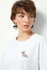 Remera blanca de corte oversize con estampa frontal pequeña de una hoja y el texto "Love Earth" en color marrón.