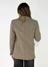 Blazer de corte clásico con solapas, cierre frontal de un botón y bolsillos laterales con solapa. Presenta una textura tejida con patrón de pequeños puntos en tonos neutros.