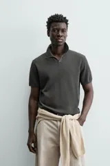 Jersey de punto color verde oliva, de calce relajado (relaxed fit), con cuello solapa y abertura frontal en forma de V. Es de manga corta y presenta acabados en rib en puños y ruedo.