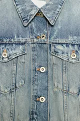 Cazadora de denim crop con cuello solapa, manga larga y cierre frontal con botones. Presenta efecto lavado, bolsillos de plastrón con solapa en el pecho y detalles de rotos.