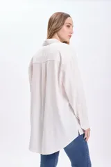 Camisa blanca de lino de manga larga con cuello clásico, cierre frontal con botones y bolsillo en el pecho.