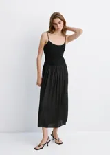 Vestido midi color negro con cuerpo ajustado de escote redondo y tirantes finos, combinado con una falda larga fruncida de tejido ligero y fluido.