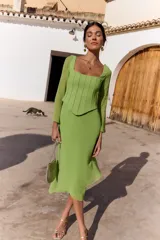 Vestido midi verde claro con efecto dos piezas, compuesto por un corset con escote cuadrado y costuras frontales estructuradas, y falda midi fluida de corte asimétrico. Cuenta con mangas largas semitransparentes.