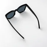 Lentes de sol Duna con armazón de policarbonato color beige y diseño rectangular con esquinas levemente angulares. Lentes oscuros con filtro UV400 y patillas gruesas.