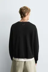 Jersey de manga larga, cuello redondo y calce relajado, color negro con efecto lavado y textura tejida.