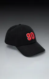 Gorra de gabardina negra con visera curva y ajuste trasero de velcro. Presenta un bordado frontal con el número "90" en color rojo con borde blanco.
