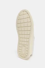 Zapatillas deportivas de mujer, color blanco hueso, con detalles en tono beige claro en el talón y paneles laterales. Presentan una suela de plataforma gruesa y cierre con cordones.