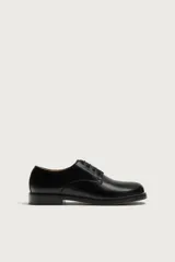 Zapato de vestir tipo derby de color negro, confeccionado en cuero con forro y plantilla de cuero, horma cuadrada y suela con ligero tacón.
