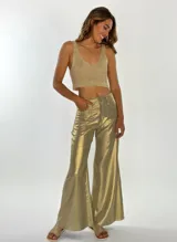 Pantalon de corte amplio y tiro alto con acabado metalizado dorado. Presenta costuras verticales frontales que estilizan la silueta y cierre frontal con botón.